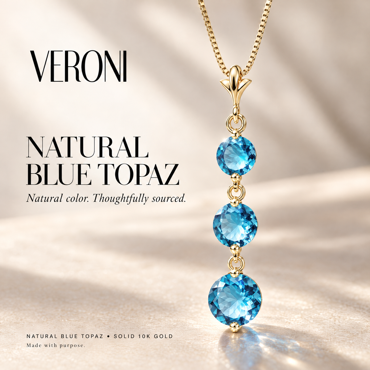 Yellow Gold Provvidenza natural blue topaz pendant on a warm ivory background in a VERONI campaign.