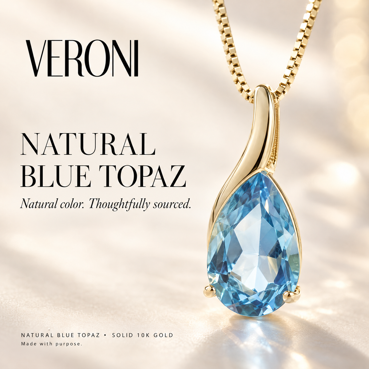 Yellow Gold Scolastica natural blue topaz pendant on a warm ivory background in a VERONI campaign.