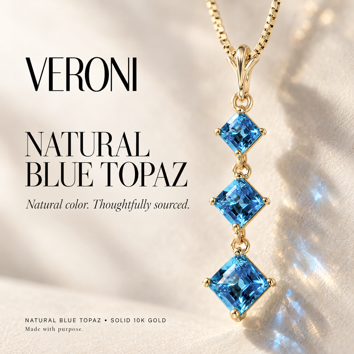Yellow Gold Pia natural blue topaz pendant on a warm ivory background in a VERONI campaign.