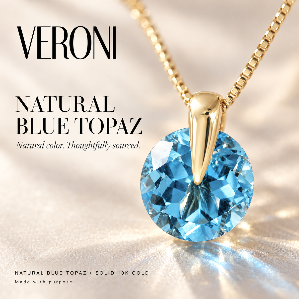 Yellow Gold Demitra natural blue topaz pendant on a warm ivory background in a VERONI campaign.